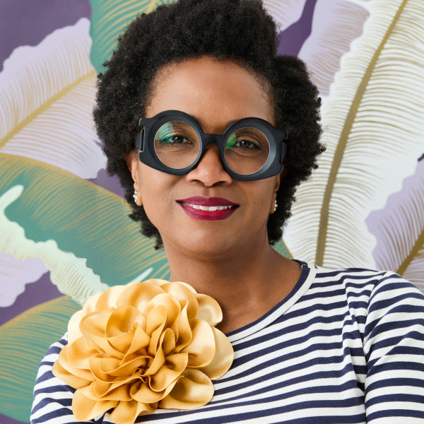 Woman wearing large black glasses with a colorful leafy background